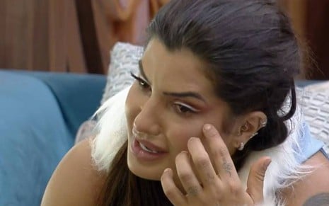 Marina chora, veste top azul e está com a mão no rosto