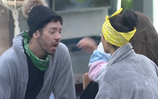Rico olha para Aline e Dayane, ele veste um roupão cinza, camiseta preta e touca preta; Aline e Dayane estão de costas e vestem seus roupões cinzas
