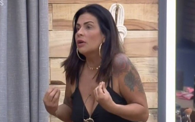 Solange olha para o lado, veste regata blusa preta e está com a boca aberta