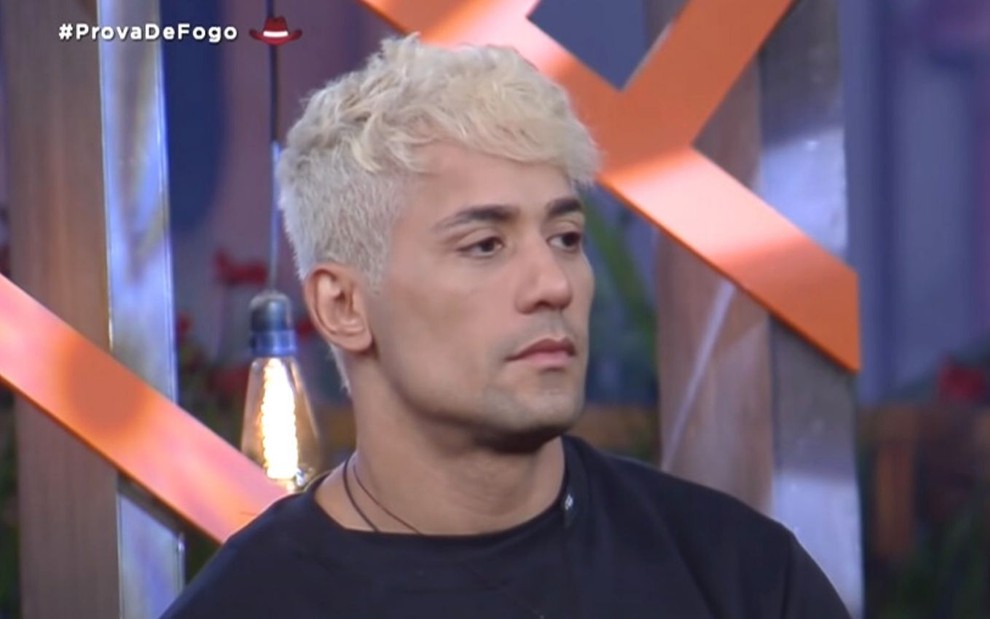 Com cabelo loiro, Tiago Piquilo usa uma camiseta preta em jogo da discórdia de A Fazenda 2021, da Record