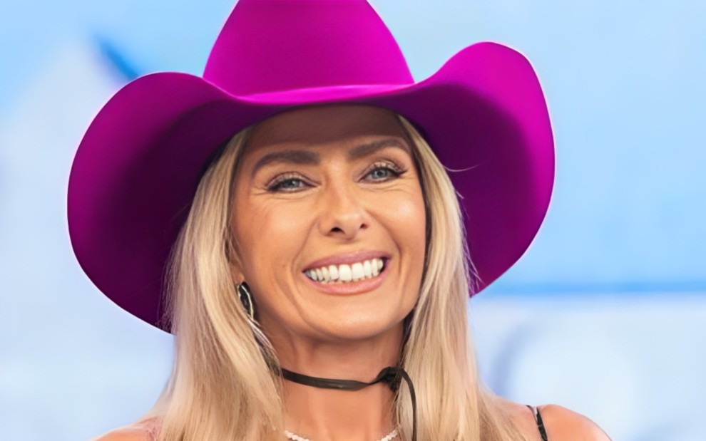 Adriane Galisteu está sorrindo, com um chapéu lilás