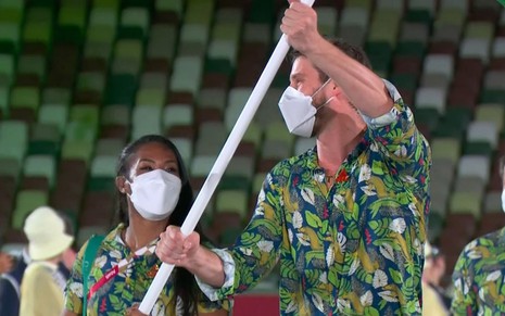 A judoca Ketleyn Quadros e o levantador Bruninho de máscara levam a bandeira do Brasil na cerimônia de abertura