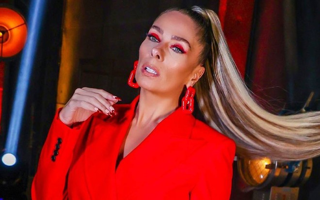 Adriane veste terno vermelho, usa brincos vermelhos e está com o cabelo preso