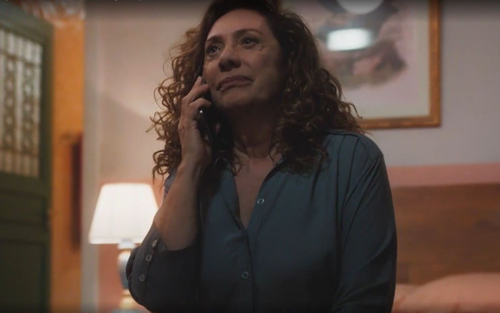 Em cena de Terra e Paixão, Eliane Giardini está conversando com alguém ao telefone