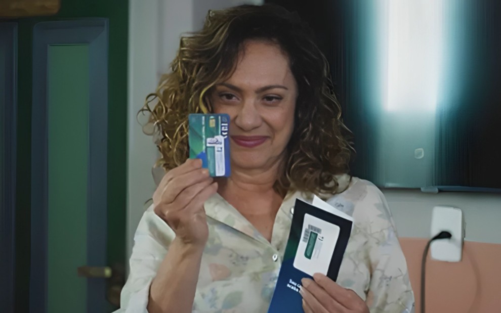 Eliane Giardini segura um cartão de crédito e está com expressão vitoriosa em cena como Agatha na novela Terra e Paixão