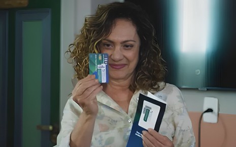 Eliane Giardini segura um cartão de crédito e está com expressão vitoriosa em cena como Agatha na novela Terra e Paixão
