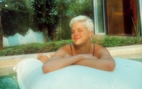 De cabelos curtinhos e platinados, Agatha Moreira sobre boia em piscina; atriz está de braços cruzados e olhando para o lado