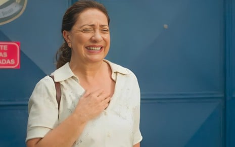 A atriz Eliane Giardini caracterizada como Agatha, chorando e sorrindo ao mesmo tempo, com mão no peito em cena de Terra e Paixão