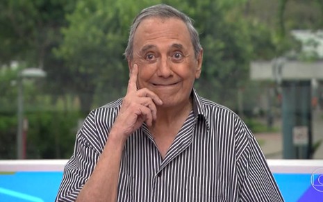 O ator Agildo Ribeiro no cenário do Vídeo Show, com sorriso de boca fechada e dedo indicador direito em riste, ao lado da cabeça