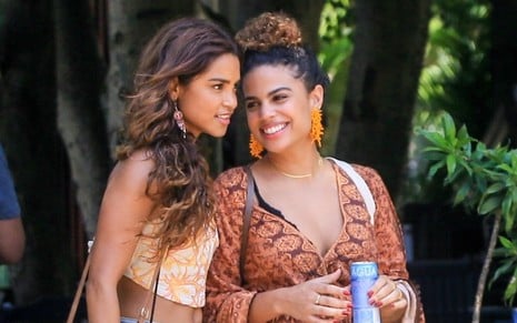 Lucy Alves anda ao lado de Clara Buarque, que sorri, em imagem registrada durante gravação da novela Travessia
