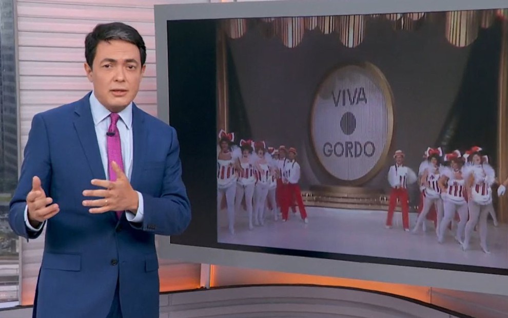 Jornalista Alan Severiano ao lado de televisão com a abertura do Viva o Gordo