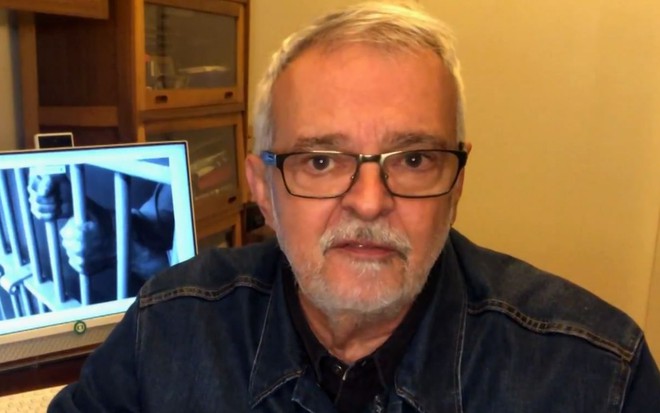 O jornalista Alberto Gaspar em reportagem gravada em sua casa, com janela e monitor de microcomputador ao fundo; material foi exibido pelo Jornal Hoje em agosto
