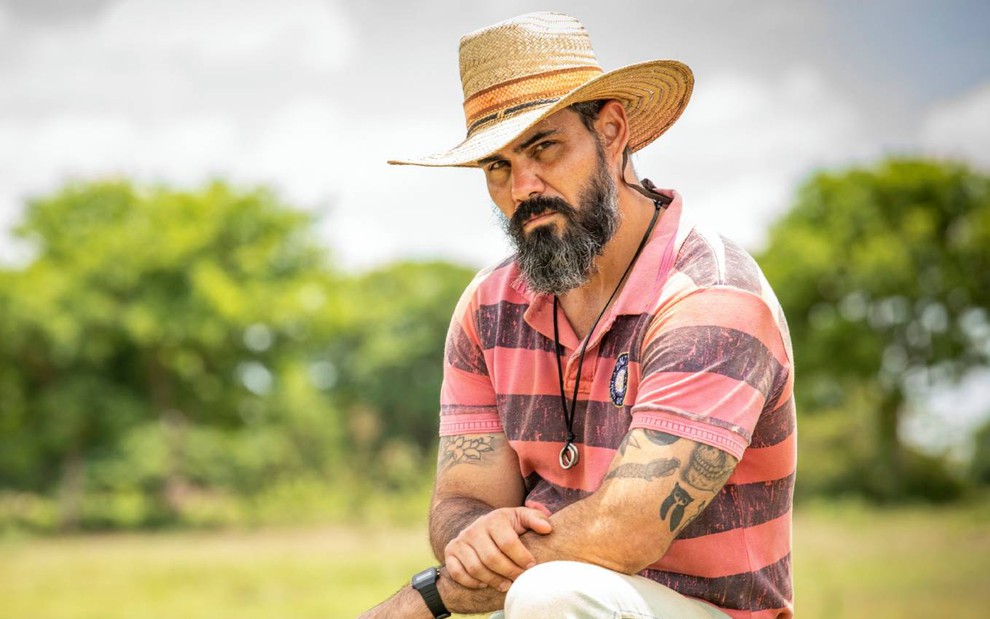 Ator Juliano Cazarré surge sentado, cruza os braços e posa para foto em cena de Pantanal