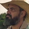 O ator Juliano Cazarré como Alcides em Pantanal; ele está de chapéu, virado para o lado olhando a paisagem com cara séria