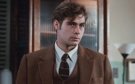 Rafael Vitti usa terno marrom e está com expressão séria em cena como Davi na novela Além da Ilusão