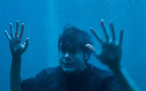 O ator Rafael Vitti como Davi em Além da Ilusão; ele está dentro de um tanque de água, com as mãos encostadas no vidro e cara de desesperado