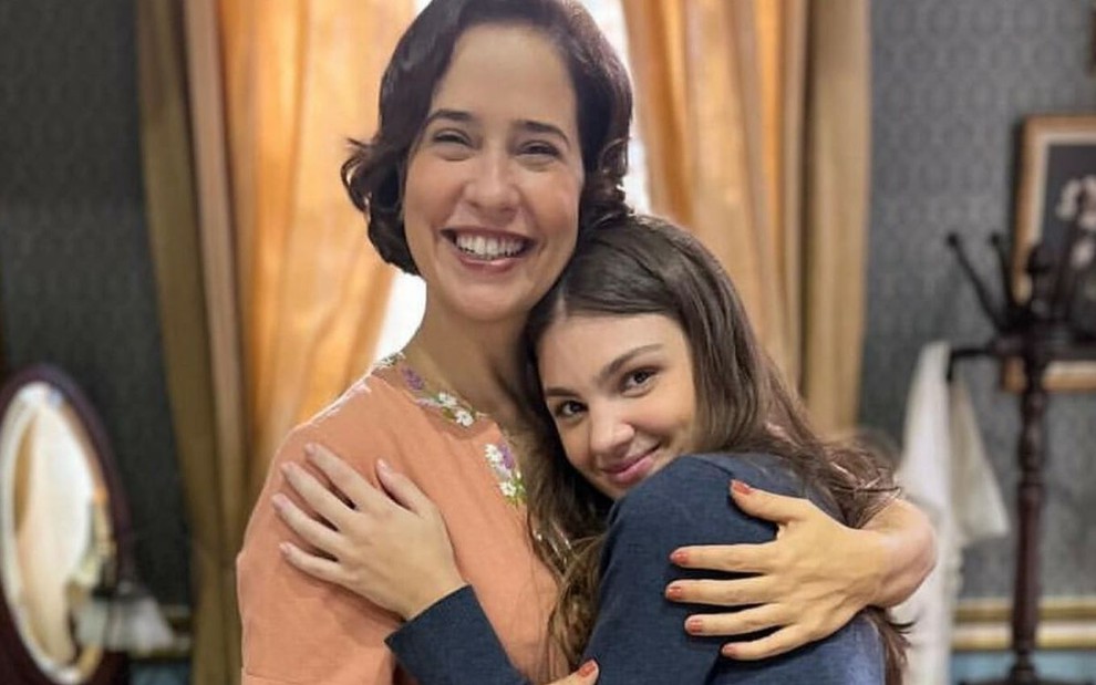 Paloma Duarte e Debora Ozório posam abraçadas caracterizadas como suas personagens em Além da Ilusão, novela das seis da Globo