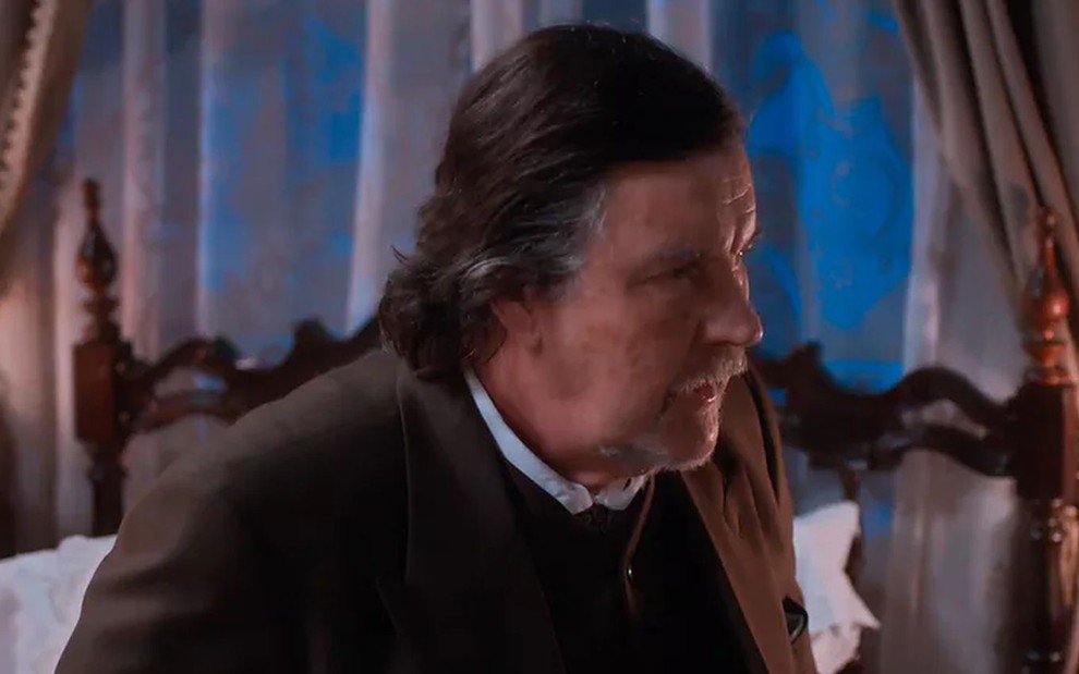 O ator Antonio Calloni como Matias em Além da Ilusão; ele está sentado de lado, olhando para a frente com cara de preocupado