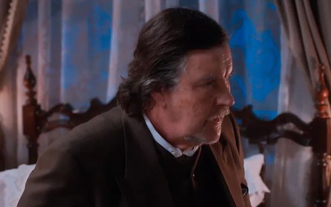 O ator Antonio Calloni como Matias em Além da Ilusão; ele está sentado de lado, olhando para a frente com cara de preocupado