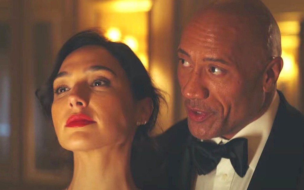 Dwayne Johnson, o The Rock, fala ao ouvido de Gal Gadot em cena de Alerta Vermelho, filme da Netflix