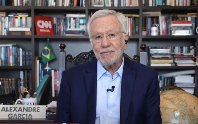 Alexandre Garcia em sua casa, com um paletó azul marinho e uma blusa azul clara, antes de ser demitido da CNN Brasil