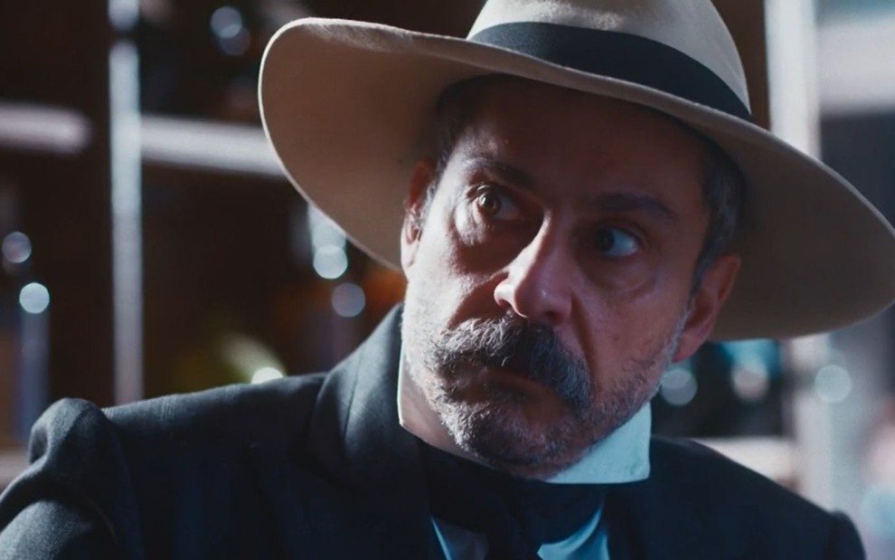 Tonico Rocha (Alexandre Nero) com expressão séria e usando um chapéu em cena da novela Nos Tempos do Imperador