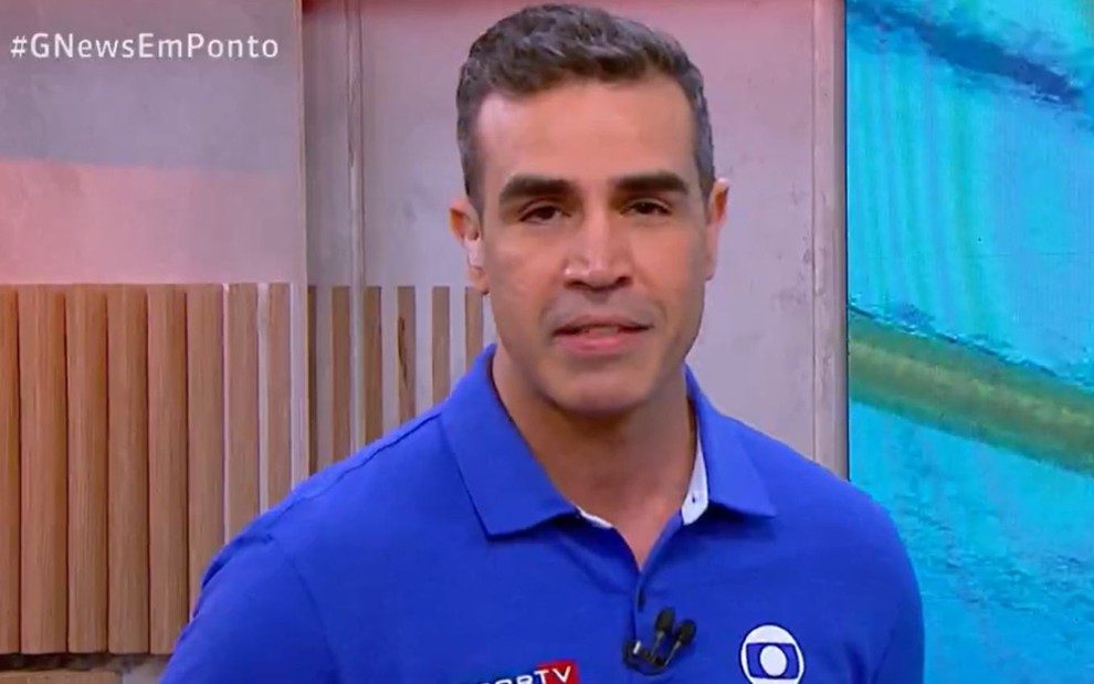 O repórter Alexandre Oliveira de camisa azul e expressão séria durante participação em telejornal da GloboNews