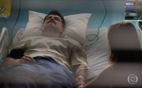 O ator Carmo Dalla Vecchia e a atriz Paolla Oliveira como Alfredo e Moa em Cara e Coragem; ele está deitado na cama do hospital, enquanto ela, de costas, segura em sua mão