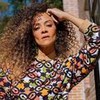 Aline Borges em foto publicada no Instagram; ela posa com um semblante sério, a mão na cabeça e veste uma camisa colorida estampada