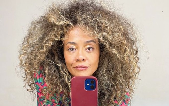 Aline Borges está com um celular na mão, em selfie no espelho