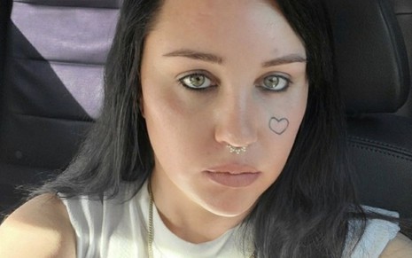 Foto atual de Amanda Bynes com cabelo preto e coração tatuado na bochecha