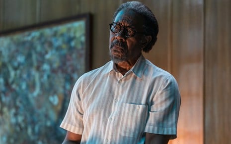 Com camisa social de manga curta e óculos de grau, o ator Clarke Peters olha para o horizonte em cena de La Fortuna