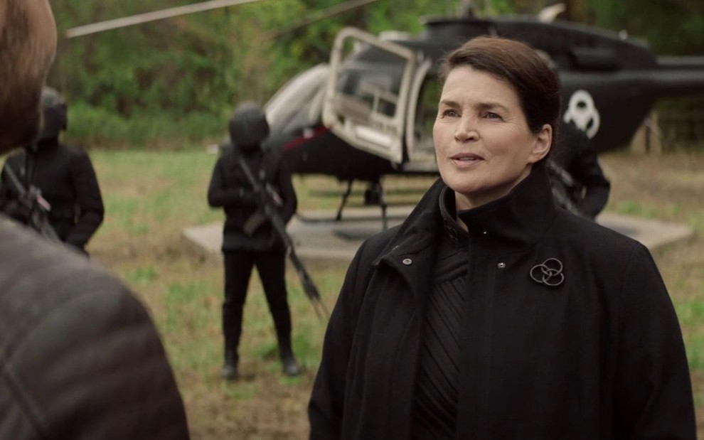 Julia Ormond veste um casaco da CRM e está em frente a um helicóptero com o mesmo logo em cena de The Walking Dead: World Beyond