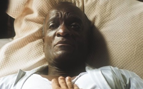 Christovam Neto deitado em uma cama em cena como Virgílio na novela Amor Perfeito