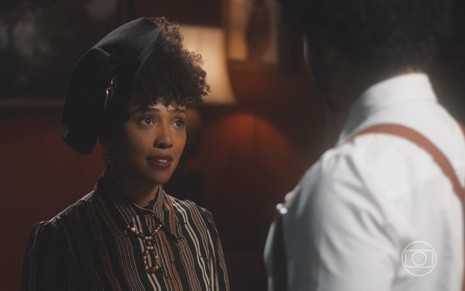 Lucília (Kênia Bárbara) em frente a Orlando (Diogo Almeida) em cena da novela Amor Perfeito, ela séria e ele de costas, os dois conversam