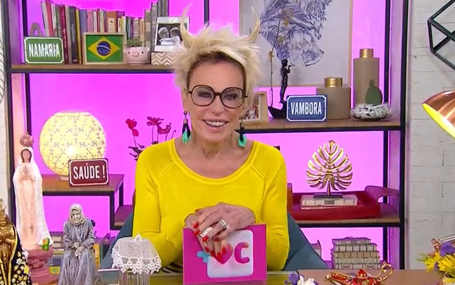 Ana Maria Braga de blusa amarela, óculos de grau, sorridente, com chifres na cabeça