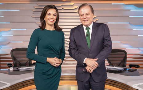 Ana Paula Araújo de roupa verde escuro, sorridente, ao lado de Chico Pinheiro, de terno cinza escuro e gravata verde
