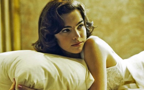 Ana Paula Arósio está deitada em uma cama e olha para o lado em cena de Hilda Furacão (1998)