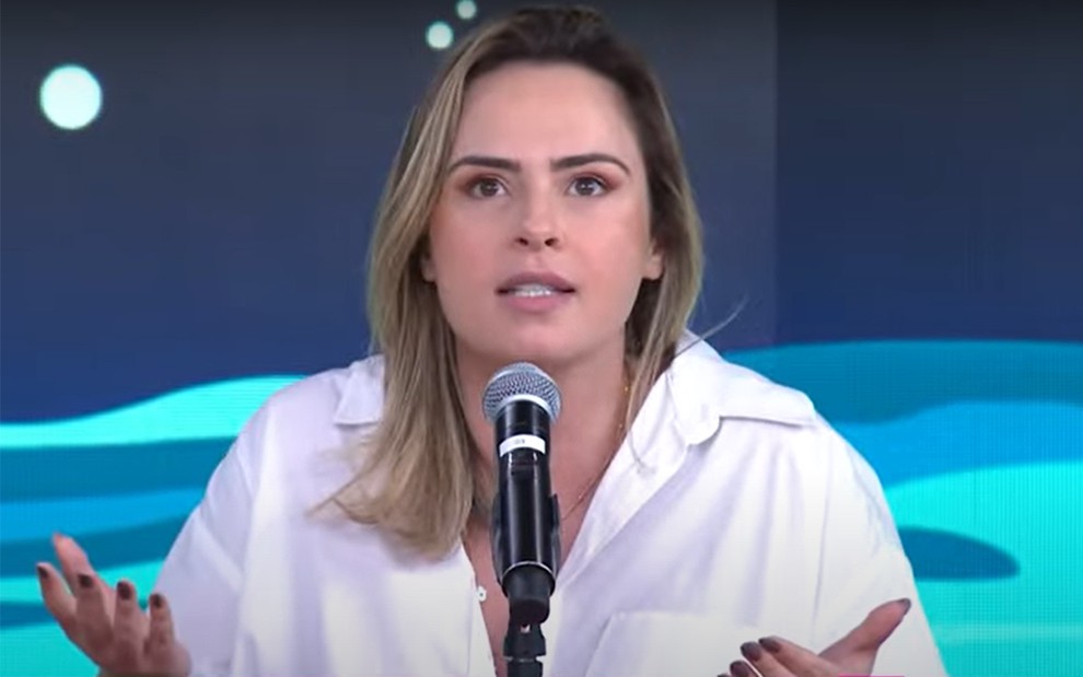 Ana Paula Renault em participação no programa Pânico da Jovem Pan, com camisa branca, expressão séria, em frente a microfone