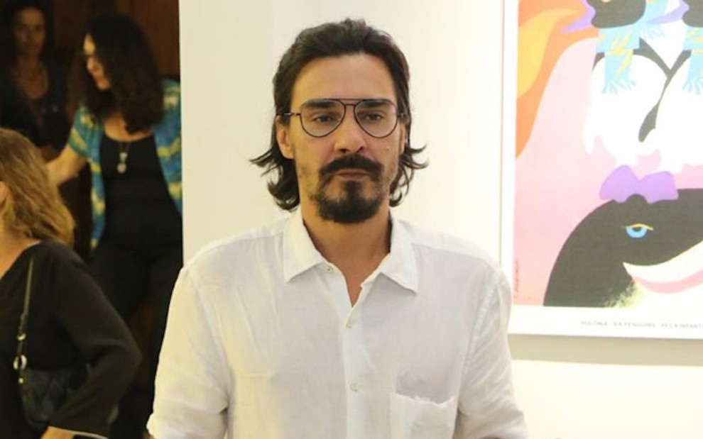 O ator André Gonçalves usa óculos e faz cara de sério ao posar para fotógrafo em evento