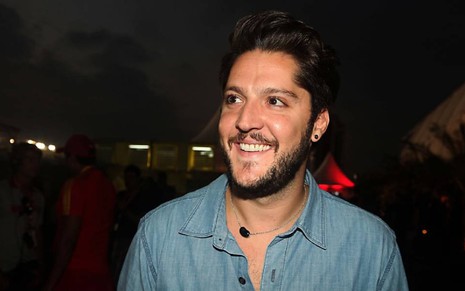 André Vasco em gravação na TV Cultura com uma camisa azul e um sorriso no rosto