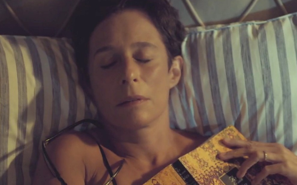 Andréa Beltrão como Rebeca em Um Lugar ao Sol; atriz está com os olhos fechados e deitada na cama