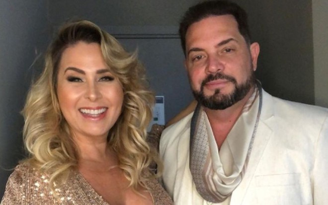 Andrea Sorvetão de blusa de paetês dourada, cabelo cacheado; Conrado de barba, camisa e blazer brancos