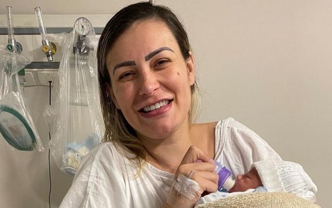 Andressa Urach no hospital em foto publicada no Instagram, ela está de avental, sorrindo e segurando o filho, Leon, no colo