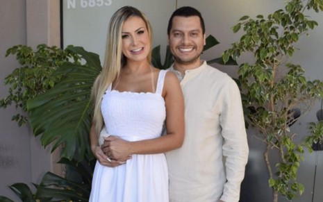 Andressa Urach e Thiago Lopes abraçados; casal veste roupas brancas em foto com plantas ao fundo