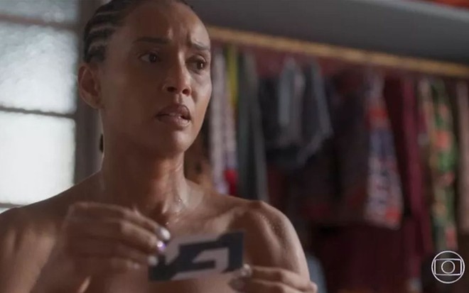 A atriz Taís Araujo como Anita em Cara e Coragem; ela está segurando um papel com as duas mãos e olhando para o lado com cara de preocupada