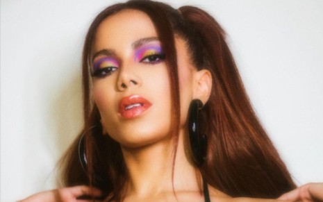 Anitta usa os cabelos presos para trás, com apenas duas mechas soltas e maquiagem lilás nos olhos