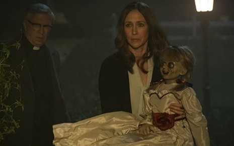 Vera Farmiga segura a boneca Annabelle no colo ao lado de Steve Coulter em cena do filme Annabelle 3: De Volta para Casa