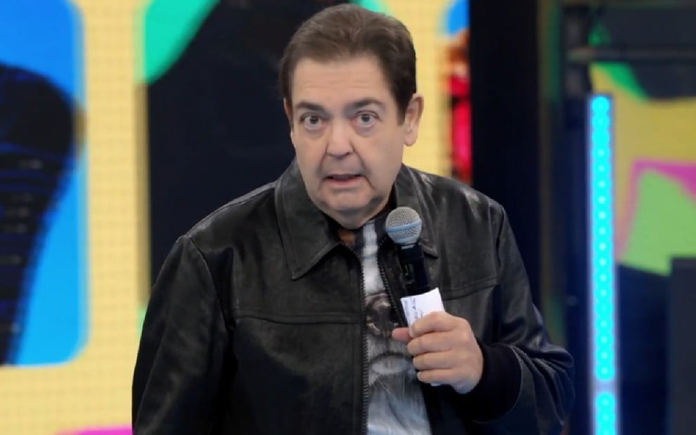 O apresentador Fausto Silva no Domingão do Faustão; ele veste jaqueta de couro e segura microfone