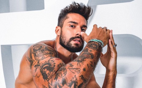 Arcrebiano de Araújo exibe suas tatuagens sem camisa, olhando de lado e com os dois braços levantados em direção ao rosto